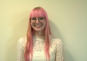Woman wearing a white lace top and long pink hair. 