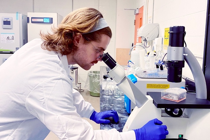 Researcher working at a laboratory bench using a microscope and scientific equipment.